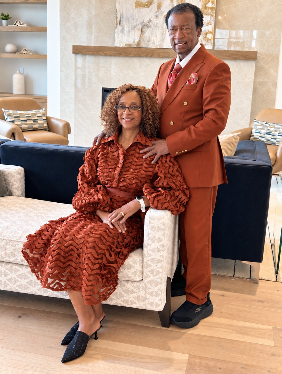 Apostle Terry L. McZeke standing beside his wife, both dressed in rust, in their living room